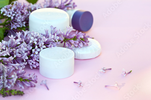 Cosmetic moisturizers creams for face and body and a fragrant soap with sprigs of blooming lilacs on a pink background. Spring tender still life. Close-up  shallow depth of field  place for text