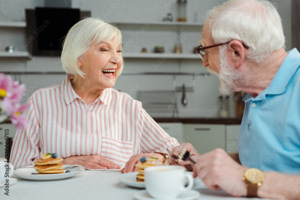 Selective focus of senior couple smiling at each other during breakfast in kitchen