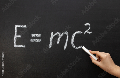 A hand writing 'E=mc2' on chalkboard. photo