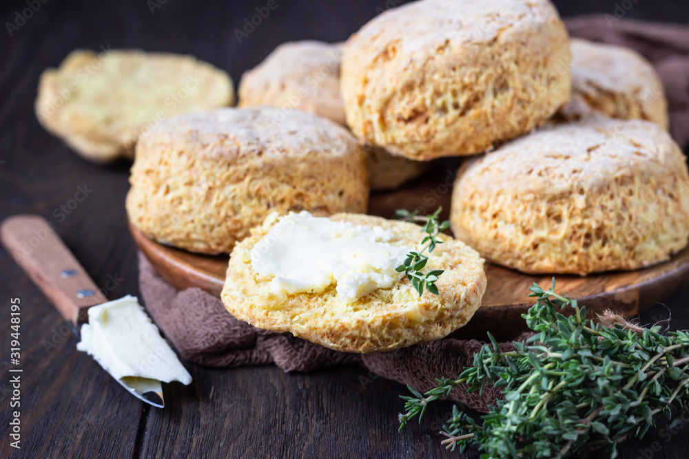 Wooden plate with English scones or buttermilk biscuits with cheese and thyme, dark brown wooden background.