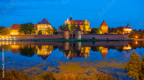 Old Teutonic Castle of Malbork reflected in river Nogat by night, Poland