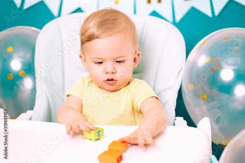 Cute baby boy sitting in his chair and playing with colorful bricks. Birthday handsome toddler child with big eyes portrait. Funny kid.