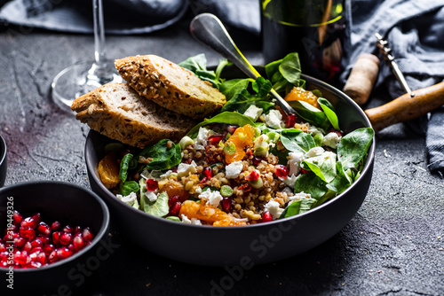 Buckwheat salad with lamb's lettuce, pomegranat seeds, goat cheese, mandarine and spring onion, Served with whole grain baguette and red wine. Black table and black background.