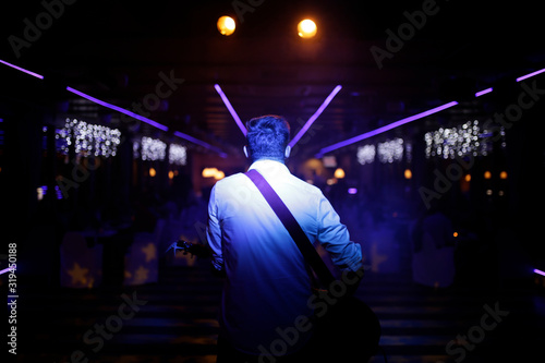 Singer with guitar at the stage. Back view ate the singer and podium. Small corporate evening. 
