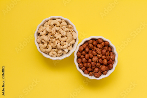 hazelnuts and walnuts in two white cups on a yellow background. lots of nuts. the concept of proper nutrition and health. Healthy food and snacks, organic vegetarian food. the view from the top. 