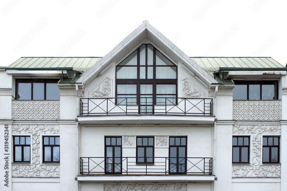 facade of a light-gray well-groomed plastered building with stucco in the form of grape leaves and circles, weaves, with ornament. Facade of a house with windows and balconies, triangular roof