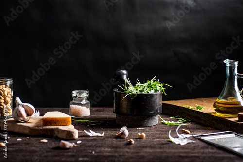 Ingredients for green arugula pesto on rustick wooden table. Stone mortar. Black background