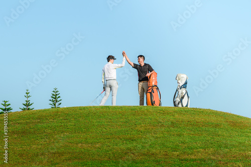 Happy golfer kneeling at hole with raised fists after putting in golf ball to the hole.