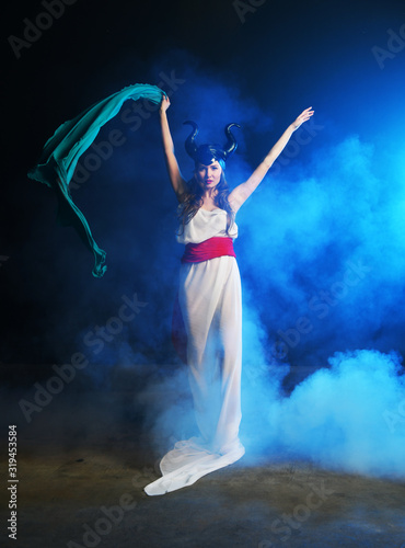 Fototapeta Naklejka Na Ścianę i Meble -  beautiful girl in the clothes of the goddess of the earth with a blue veil on a background of smoke