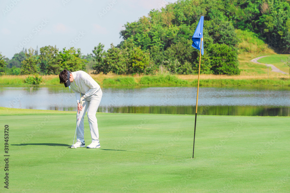 Obraz premium Sport Healthy. Golfer asian sporty woman focus putting golf ball aim on outdoor the green golf on sunset evening relax time. Healthy and Lifestyle Concept