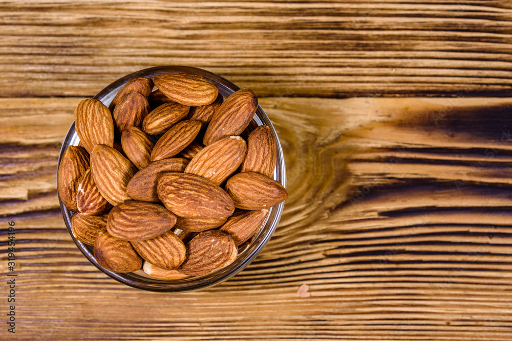 Glass bowl with the peeled almond nuts on wooden table. Top view Glass bowl with the peeled almond nuts on wooden table. Top view