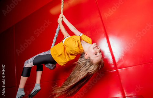 Happy child girl swinging on rope in indoor playground center