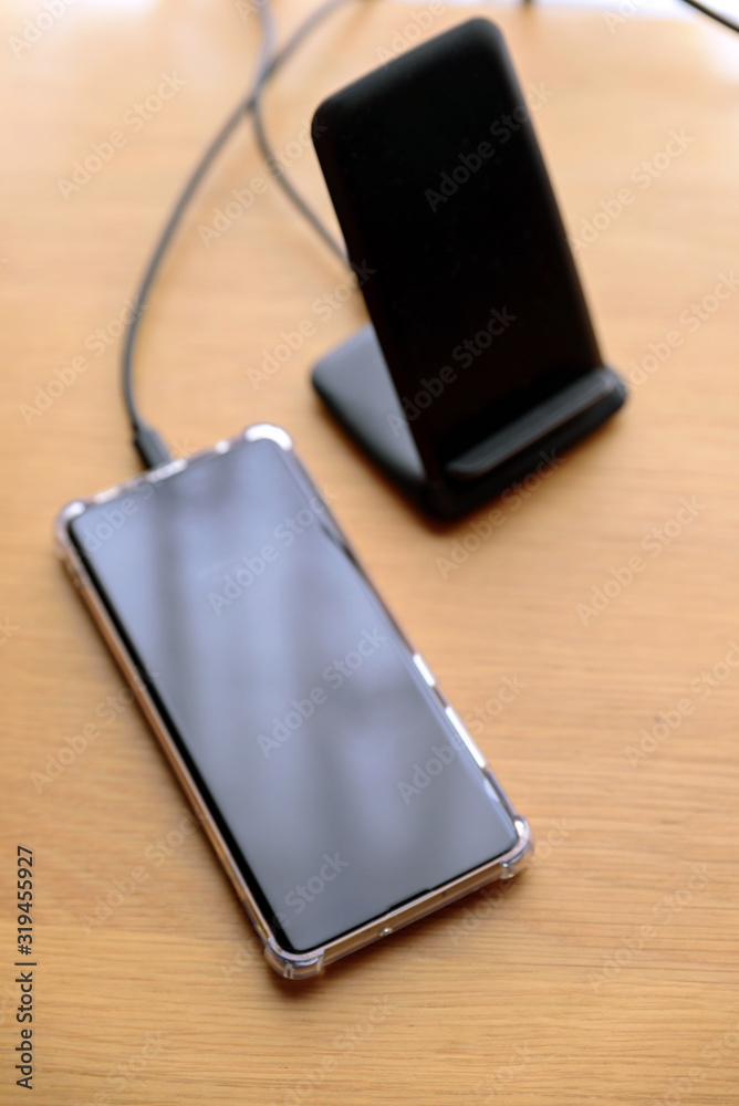 smartphone wireless charging on charging stand on wooden table smartphone wireless charging on charging stand on wooden table