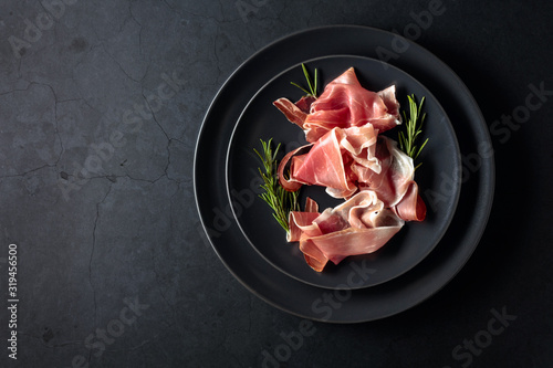 Prosciutto and rosemary on a black plate. Top view. photo