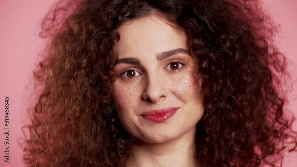 Young curly woman with trendy glitter freckles make-up. Portrait of flirting beautiful girl on pink studio background. Young curly woman with trendy glitter freckles make-up. Portrait of flirting beautiful girl on pink studio background.