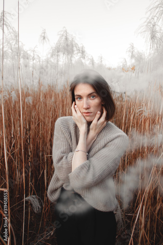 A beautiful model girl with a Scandinavian appearance. girl traveler blogger in a beige sweater in an open space among the fluffy grass. Soft background, very sensual photo