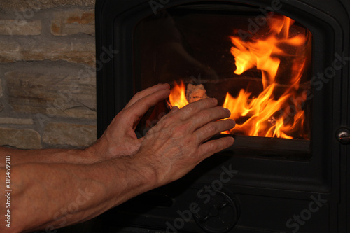 middle-aged man sitting near a hot burning fireplace, arms outstretched to the fire, winter mood concept