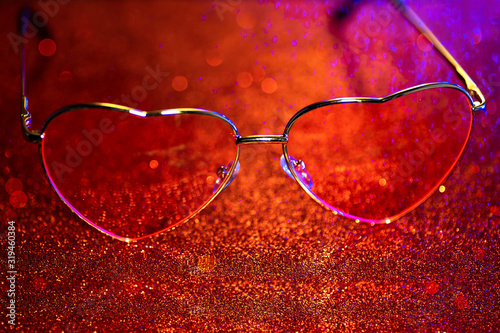 Heart-shaped glasses on a red background with bokeh. The Valentine's Day concept