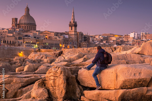 Man sitting on the rock and watch beautiful architecture of the Valletta city at dawn, Malta