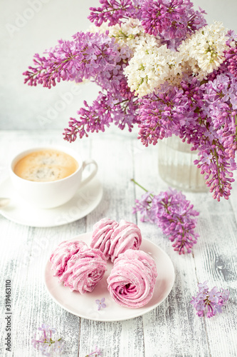 Lilac, coffee and homemade pink marshmallow on white ceramic plate. Romantic spring morning. Selective focus