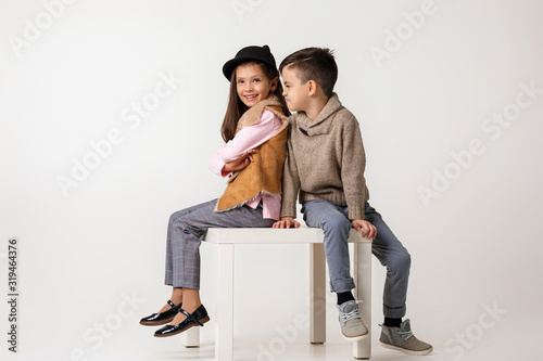 Cute stylish little couple girl and boy in fashionable clothes sittting together at studio. child boy hugs girl and tells her a funny story. kids fashion concept.
