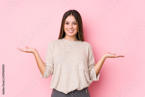 фотографія Young caucasian woman posing isolated makes scale with arms, feels happy and confident