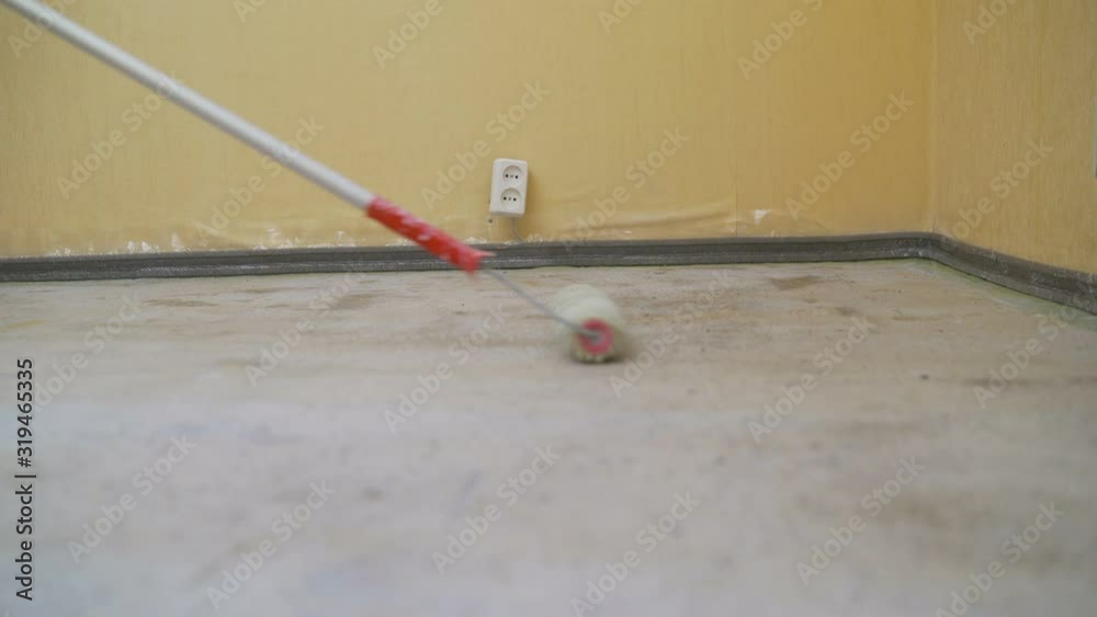 Worker puts primer with roller on concrete floor in room from unfinished apartment. Repair in the apartment, primer floors with a roller Worker puts primer with roller on concrete floor in room from unfinished apartment. Repair in the apartment, primer floors with a roller