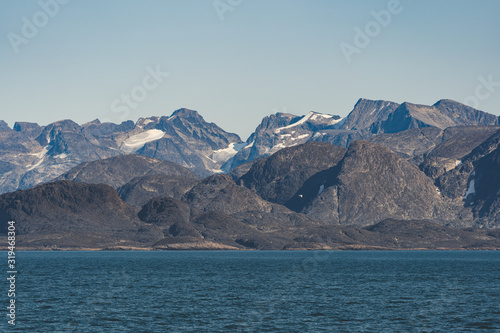 Arctic landscape of Greenland on a sunny day in Summer. Beautiful view of mountains with Snowy peaks and Glaciers along the Atlantic Ocean.