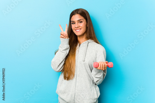 Young fitness woman holding a weight showing victory sign and smiling broadly.