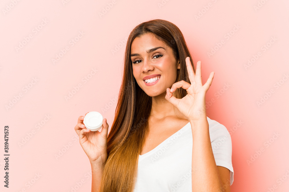 Young caucasian woman holding a moisturizer cheerful and confident showing ok gesture. Young caucasian woman holding a moisturizer cheerful and confident showing ok gesture.