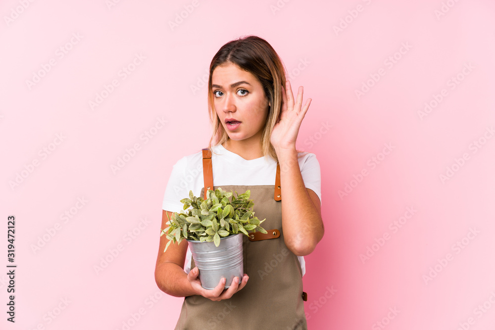 Young caucasian gardener woman in a pink background trying to listening a gossip. Young caucasian gardener woman in a pink background trying to listening a gossip.