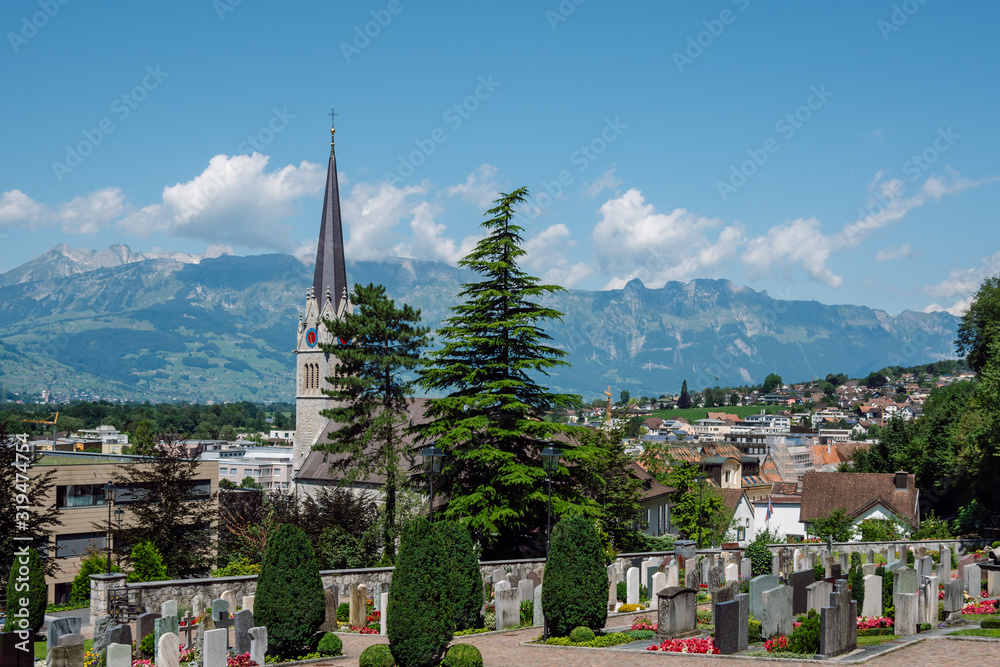 During a clear sunny day view of the Vaduz Cemetery, St. Florin Catholic Cathedral in the background are the Swiss Alps.