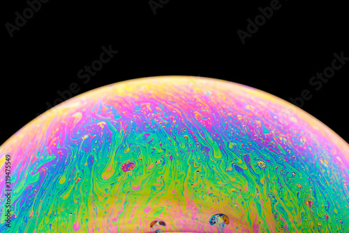 Rainbow soap bubble on an isolated black background. Close-up of the colorful surface. Poster blank