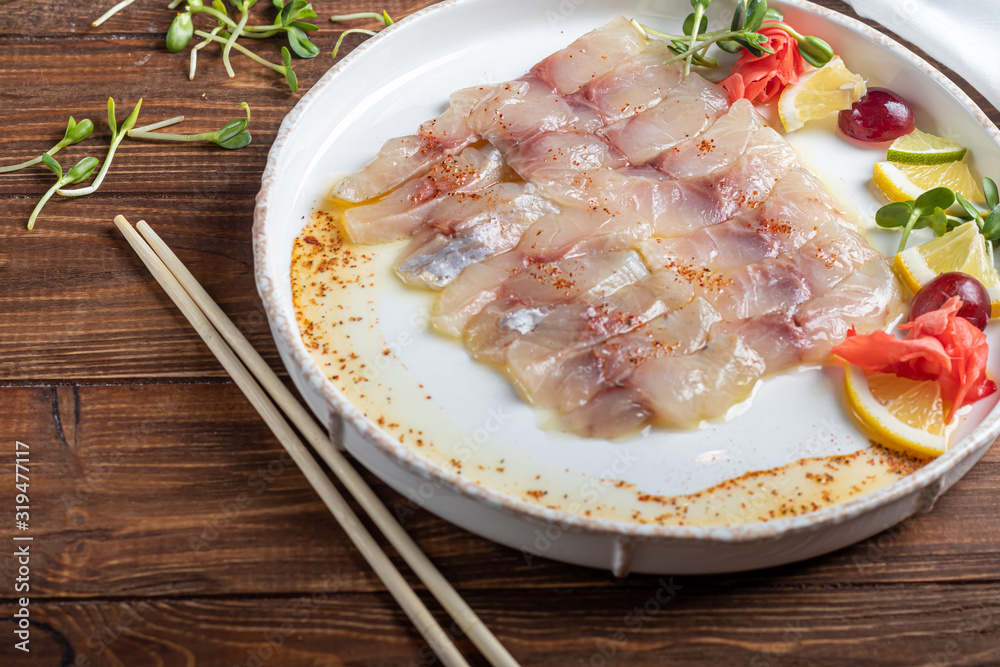 Light-salted dorado with sunflower in truffle oil. Next to slices of lemon, lime, grapes, pickled ginger. To the side of the plate are chopsticks. Light-salted dorado with sunflower in truffle oil. Next to slices of lemon, lime, grapes, pickled ginger. To the side of the plate are chopsticks.