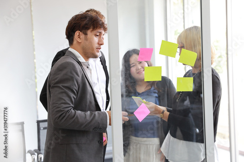 Multiethnic business people using post it notes for brainstorming together with information from colleague in meeting room. Business people team standing and working on new startup project.