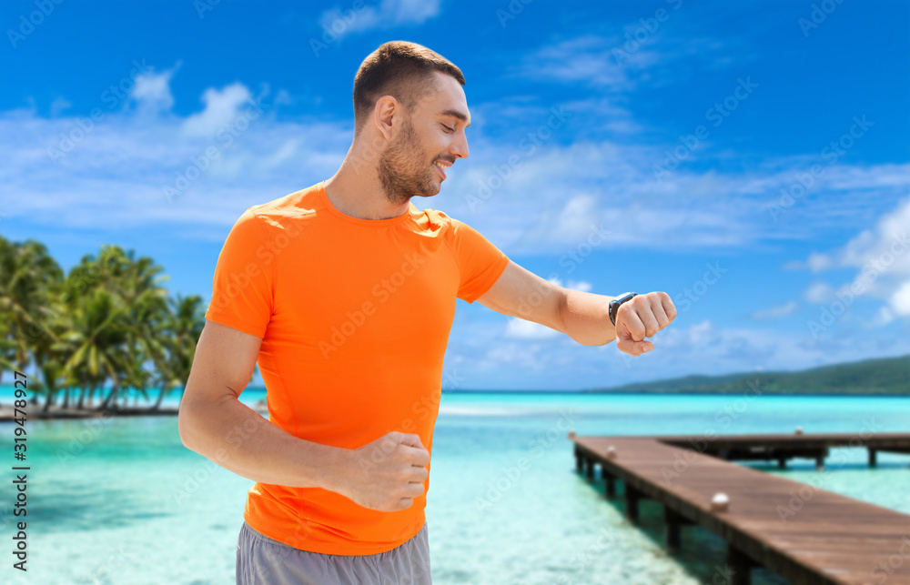 sport, technology and people concept - smiling young man with smart watch or fitness tracker at summer over city street on background sport, technology and people concept - smiling young man with smart watch or fitness tracker at summer over city street on background