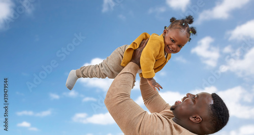 family, fatherhood and people concept - happy african american father playing with baby daughter over blue sky and clouds background