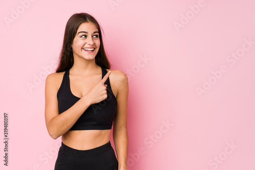 Young caucasian fitness woman doing sport isolated smiling and pointing aside  showing something at blank space.