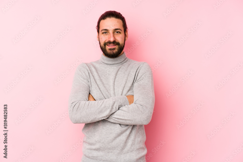 Young long hair man isolated on a pink background who feels confident, crossing arms with determination. Young long hair man isolated on a pink background who feels confident, crossing arms with determination.
