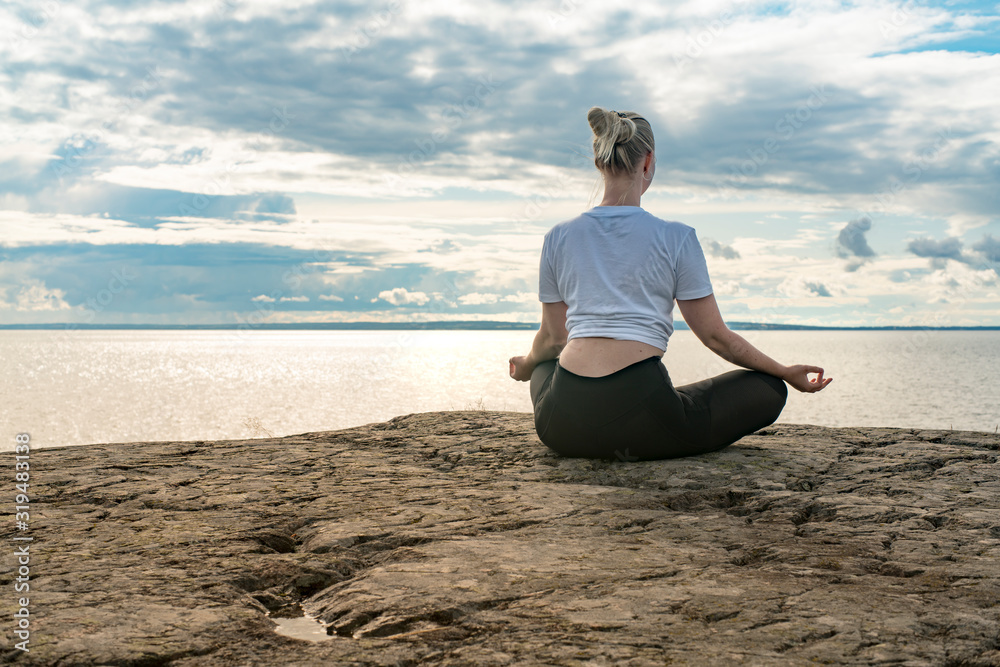 Woman practicing Yoga, meditation or stretching close to water on Cliff doing different poses on beautiful landscape. Concept of finding ideal calm meditation place, finding yourself and Healthy Life.