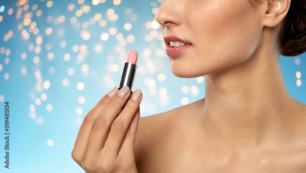 beauty, makeup and cosmetics concept - happy smiling young woman with pink lipstick over holidays lights on blue background beauty, makeup and cosmetics concept - happy smiling young woman with pink lipstick over holidays lights on blue background