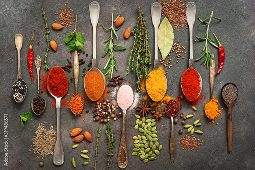 A variety of spices, herbs, seeds in a spoon on a dark painted rustic background. Assorted colored different seasonings. Flat lay,view from above.