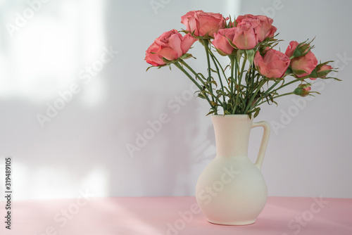 Bouquet of red roses in vase on a pink table on beige background with soft sunlight. Copy space