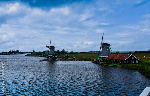 Zaanse Schans, Holland, August 2019. Northeast Amsterdam is a small community located on the Zaan River. View of the mills on the river bank, they stand out with their bright colors. Cloudy day.