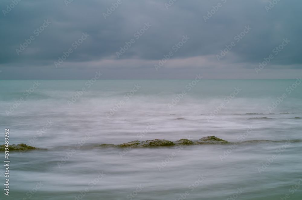A long exposure black sea and a large green rock above the water look like fog A long exposure black sea and a large green rock above the water look like fog
