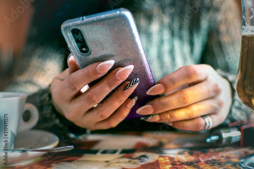 Woman's hands with manicured nails holding smartphone in the cafe