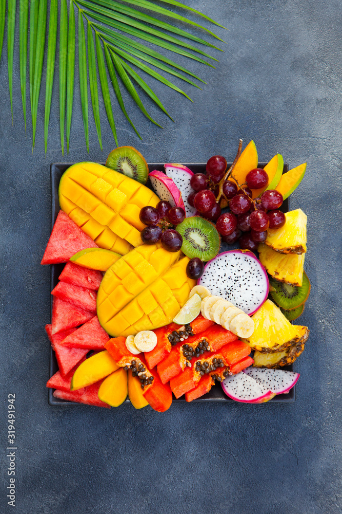 Tropical fruits assortment on a plate. Grey background. Top view.