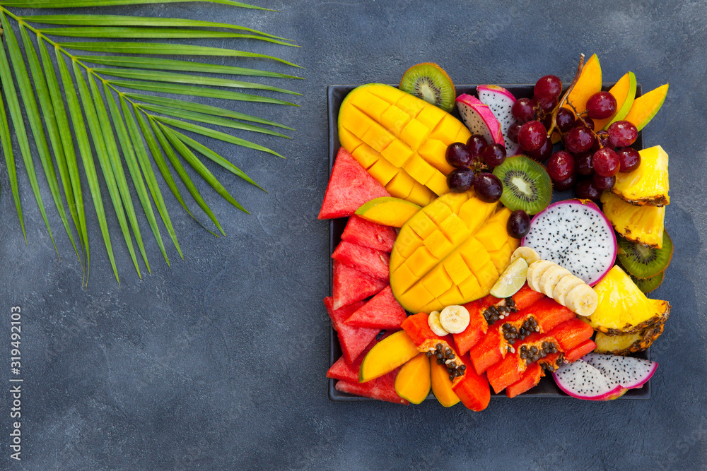 Tropical fruits assortment on a plate. Grey background. Copy space. Top view.