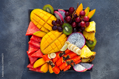 Tropical fruits assortment on a plate. Grey background. Close up. Top view.