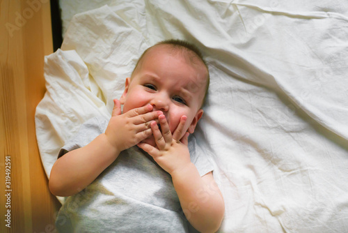 Fotografie Cute boy is lying on a white pillow and crying through his teeth